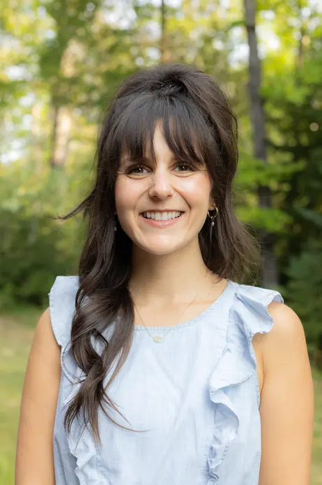 Smiling woman outdoors with a blurred forest background.
