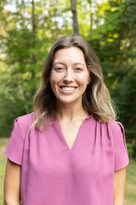 Smiling person in a pink shirt, with trees in the background.