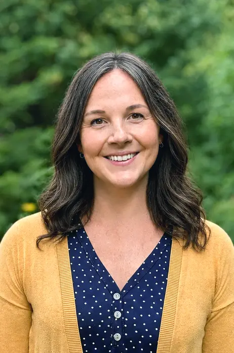 Smiling woman in a yellow cardigan, outdoors with a green background.