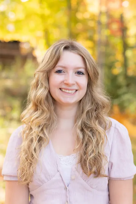 Smiling woman with curly hair, outdoors in autumn scenery.